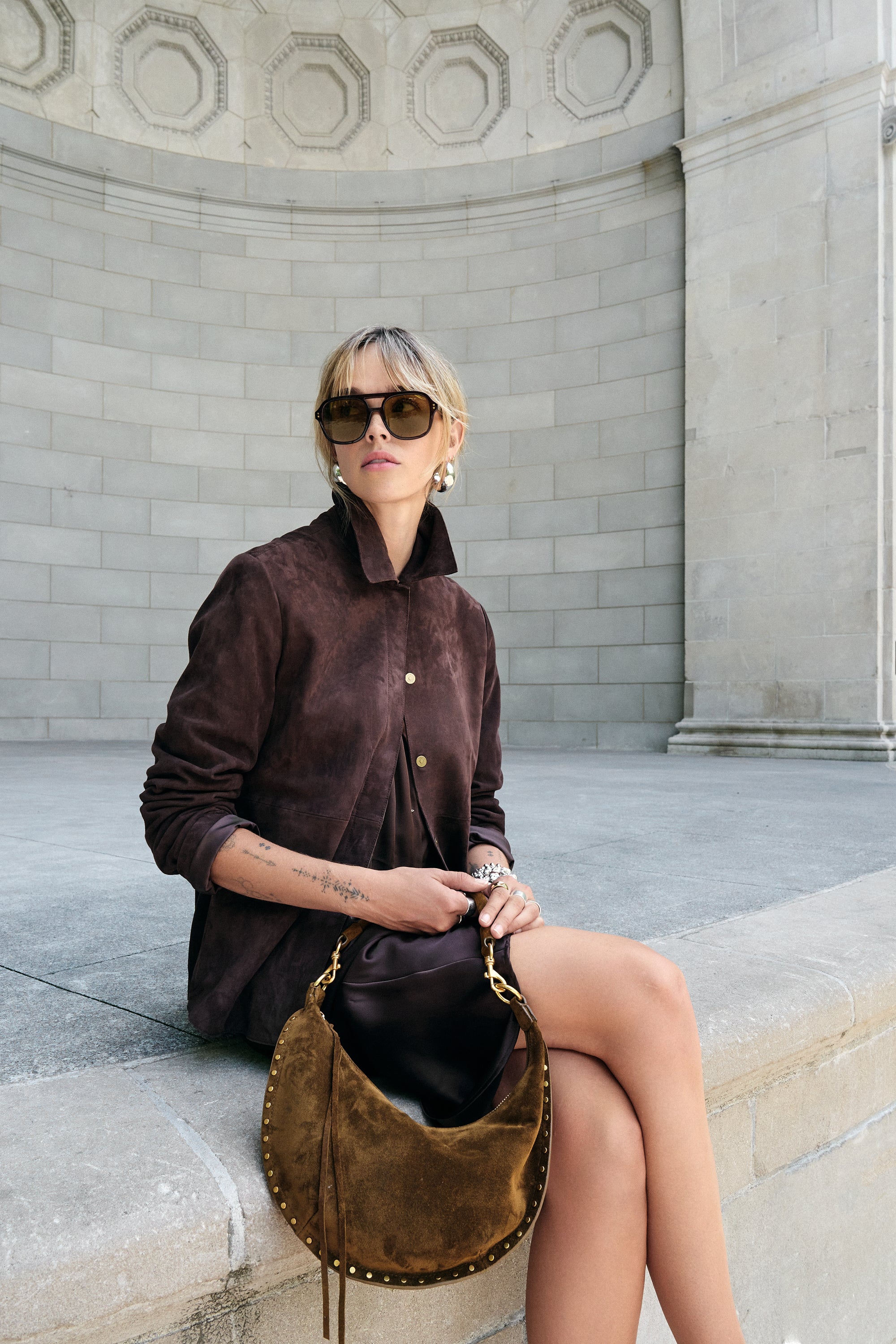 Woman in a brown outfit sitting on stone steps holding a brown handbag.